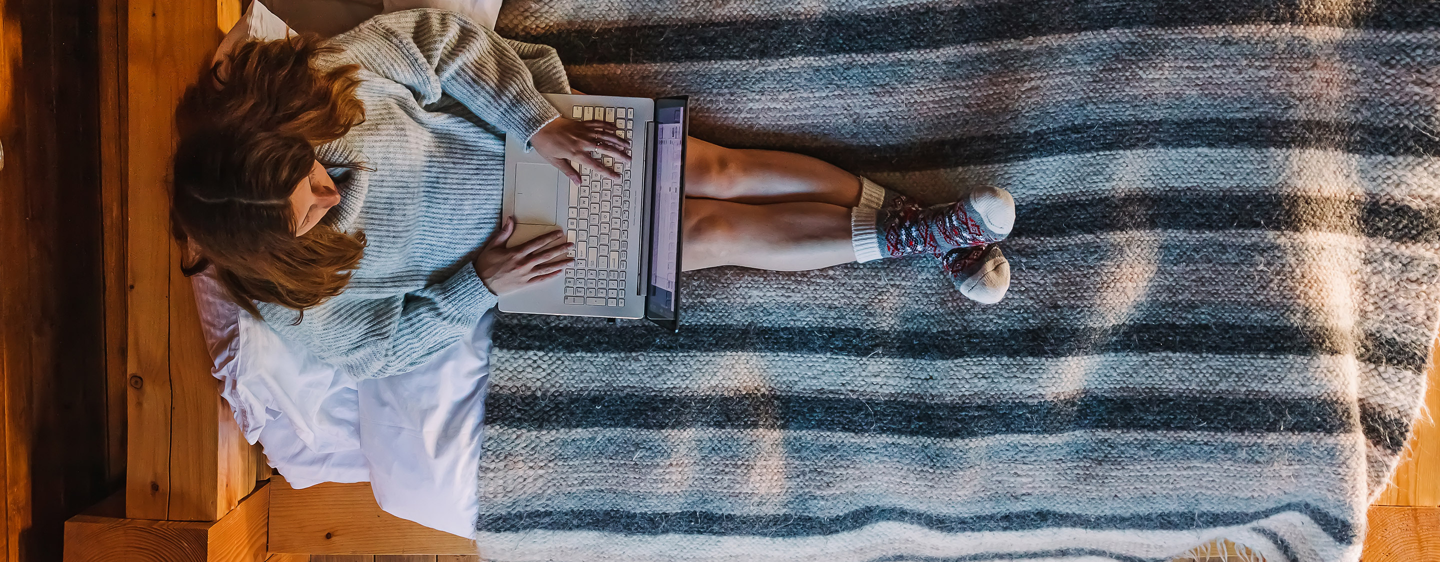 Frau die auf einem gemütlichen Bett am Laptop sitzt - Tuja Reisen Newsletter